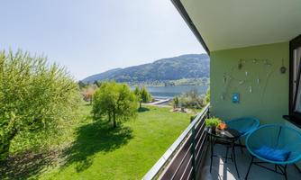 A beautiful balcony with a view of a green meadow and the lake. In the background, gentle hills and a clear sky can be seen.