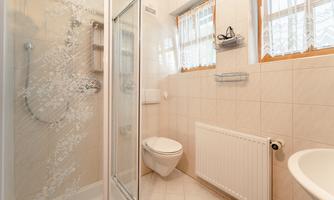 A modern bathroom with a shower, a toilet, and a sink. The walls are light-colored tiled and there are windows for daylight.