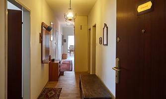 A bright hallway with wooden floors and walls in neutral colors. At the end of the hallway, a dining area is visible.