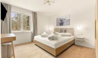 A cozy bedroom with a double bed and large windows. On the wall hangs a picture of a cow, and the room is brightly and cheerfully decorated.