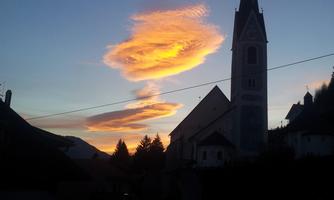 A picturesque sunset with orange clouds over a church. The silhouette of the buildings is visible in the foreground.