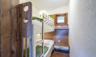 A small room with a wooden bunk bed. The walls are bright, and the windows let in plenty of light.
