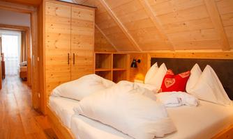 A cozy bedroom with a wooden ceiling and a large bed. The walls are kept light, and the room radiates a warm atmosphere.