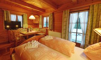 A cozy wooden fire room with two beds and a dining area. Large windows provide a view of the outdoor area.