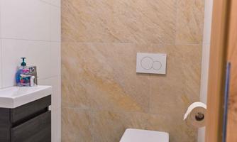A modern bathroom with a flat toilet and a small sink. The walls are decorated with light tiles and an attractive stone pattern.