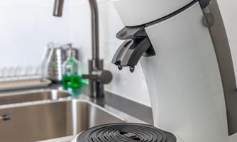 A modern coffee machine is on a kitchen counter next to a sink. It has an elegant design in white and black.