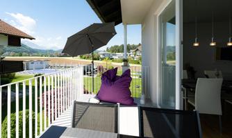 A beautiful balcony with a purple bean bag and a sun umbrella. In the background, green meadows and mountains can be seen.