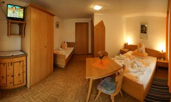A cozy room with two beds, a wooden table, and a television. The warm color tone of the furniture creates an inviting atmosphere.