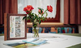 A table with a glass of flowers that contains red roses. Next to the bouquet lies a folder and some brochures.