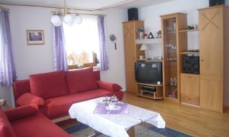 A cozy living room with red sofas and a large window cutout. A table with flowers and a television are also visible in the room.