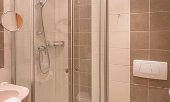 A modern bathroom with a shower and glass door. The walls are designed with tiles in neutral colors.