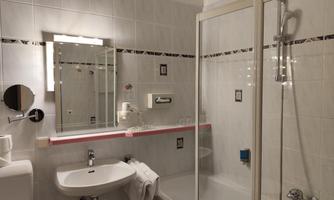 A modern bathroom with a shower, sink, and mirror. The walls are brightly tiled and there are some bath accessories.