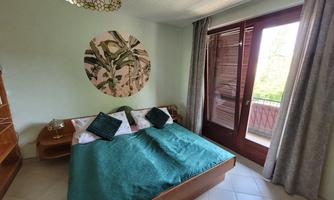 A cozy bedroom with a large bed and colorful cushions. Large windows offer a view outside.