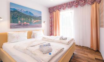 A cozy bedroom with a large bed and bright curtains. A picture of a picturesque landscape hangs on the wall.