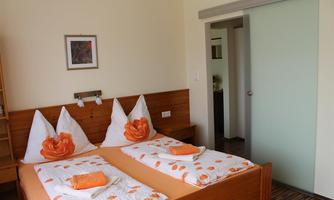 A cozy bedroom with a double bed and orange accents. The walls are bright and there is a modern sliding door closet.