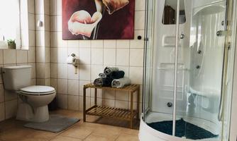 A modern bathroom with a shower, a toilet, and a wooden shelf. A picture of flowers hangs on the wall, and fresh towels are neatly stacked.