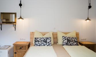A cozy bedroom with two beds and bright bedding. Stylish lamps and a small mirror hang on the wall.
