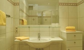 A modern bathroom with bright tiles and a large mirror. Yellow towels and a vanity are visible.
