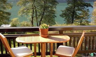 A cozy table with two chairs on a terrace. In the background, there are trees and a peaceful lake.