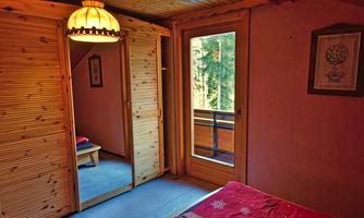 A cozy bedroom with wooden furniture and a large window. The view overlooks a balcony that is surrounded by trees.