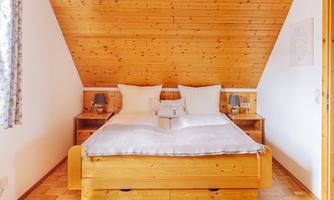 A cozy bedroom with wooden paneling and a large double bed. Next to the bed are two nightstands with lamps.