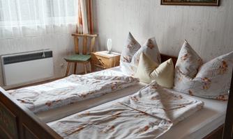 A cozy bedroom with two beds and floral bedding. A picture hangs on the wall, and a small table stands next to the beds.