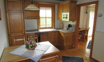 A cozy kitchen with wooden cabinets and a small dining area. Plenty of daylight comes through the window, creating an inviting atmosphere.