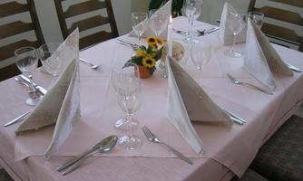 A festively set table with a pink tablecloth. The decoration consists of a floral arrangement and elegant cutlery.