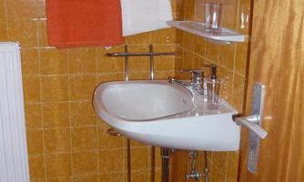 A small bathroom with orange towels and tiles. A modern sink is in the corner.