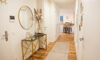 A modern hallway with a round mirror and an elegant table. In the background, a person is standing at a table in a bright room.