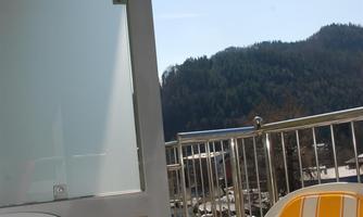 A balcony with two yellow chairs and a table. In the background, green hills and a blue sky can be seen.