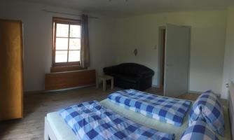 A simple room with two beds and plaid blankets. There is a sofa and a window with plenty of daylight.