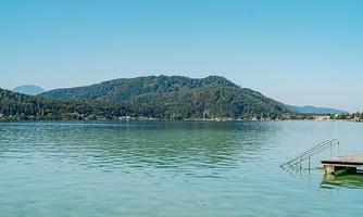 A tranquil lake with clear water and gentle green hills in the background. The sky is blue and cloudless.