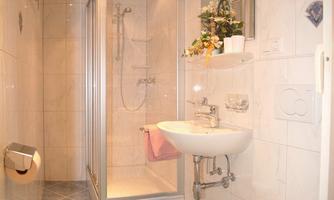 A modern bathroom with a bright tiled floor and a shower. There are flowers and towels on the sink.