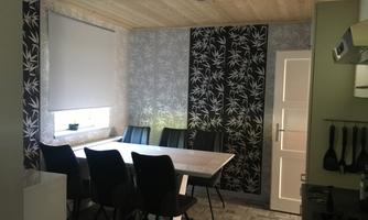 A modern kitchen with a large dining table and black chairs. The walls are decorated with floral patterns and neutral colors.