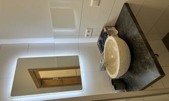 A modern bathroom with a round stone sink. The area is bright and designed in a minimalist style, featuring a lit mirror and an elegant black countertop.