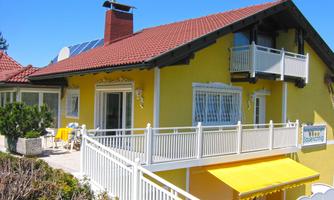 A sun-yellow painted house with a red roof and white balconies. Yellow furniture is placed on the terrace, and a sunny atmosphere invites you to relax.