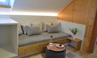 A cozy living area with a modern upholstered sofa and a table. The walls are made of wood, and there are fresh flowers on the table.