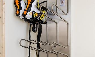 A modern shoe rack made of stainless steel with multiple compartments. At the top, there is a pair of ski boots and below is a pair of sneakers.