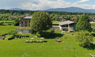 A green landscape with several buildings and trees. In the foreground, there are loungers and a playground.