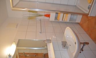A modern bathroom with a shower and a sink. The walls are tiled and there are colored towels on a shelf.