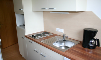 A modern kitchen with a wooden countertop, a sink, and a coffee machine. The kitchenette is bright and well-organized.