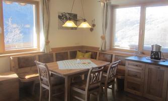 A cozy dining kitchen with a wooden table and benches. Large windows provide plenty of daylight.