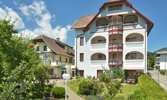 A beautiful building with red accents and balconies in a green environment. In the foreground, there is a well-maintained garden with plants.