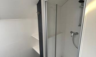 A modern shower in a bathroom. The walls are kept in a bright white, and the floor is tiled in dark.