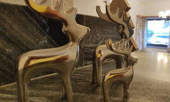 Three stylized deer figures made of metal stand on a table. In the background, a window can be seen, showing a cozy room.