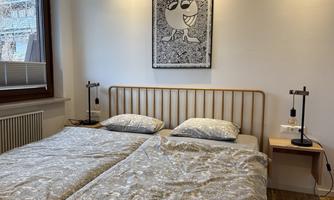 A cozy bedroom with two beds, beautifully decorated with bedding and nightstands. An artistic picture hangs on the wall.