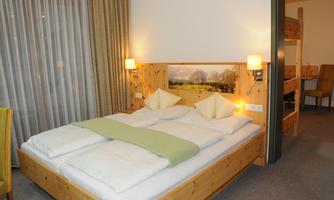 A cozy room with a large bed and wooden decor. There are warm colors and a relaxed atmosphere.