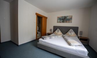 A simple bedroom with a large bed and two pillows. In the background, there is a door to the bathroom and a decorative picture on the wall.