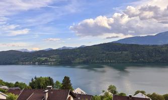 A peaceful landscape with a lake and gentle hills in the background. The sky is partly cloudy with a clear blue.